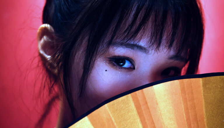 mujer asiática tapando media cara con un abanico amarillo